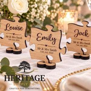 May include: Three light brown wooden puzzle piece place cards standing on small bases. Each piece is engraved with a name, the text Mr & Mrs Smith, and the date 14th July 2024. The names Louise, Emily, and Jack are featured in a script font.
