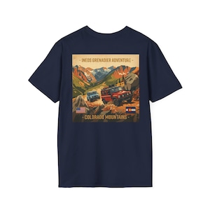 Puede incluir: Una camiseta azul marino con un gráfico en la parte posterior. El diseño muestra dos vehículos todoterreno en un paisaje montañoso con el texto INEOS GRENADIER ADVENTURE y COLORADO MOUNTAINS, junto a una bandera de EE. UU. y de Colorado.