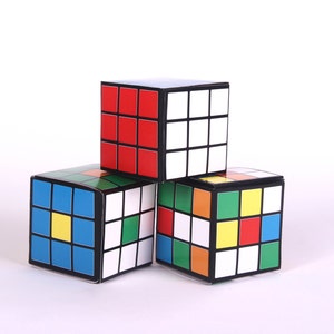 May include: Three colorful cube-shaped boxes stacked on top of each other. The top box is red, white, and black. The middle box is blue, yellow, and green. The bottom box is red, yellow, blue, and green.