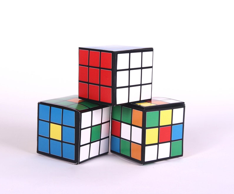 May include: Three colorful cube-shaped boxes stacked on top of each other. The top box is red, white, and black. The middle box is blue, yellow, and green. The bottom box is red, yellow, blue, and green.