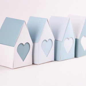 Puede incluir: Cuatro casas de papel azul claro y blanco con recortes en forma de corazón. Las casas están dispuestas en fila de izquierda a derecha.