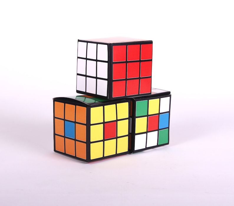 May include: Three colorful cube-shaped boxes stacked on top of each other. The top box is red and white, the middle box is green and white, and the bottom box is orange, yellow, blue, and white.