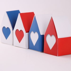 May include: Four small houses made of cardboard, each with a heart-shaped window. The houses are painted in red, white, and blue.