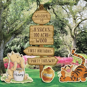 Könnte beinhalten: Ein Holzschild mit vier Wegweisern mit der Aufschrift WELCOME TO, JESSICA'S 100 ACRE WOOD, FIRST BIRTHDAY und PARTY THIS WAY. Neben dem Pfosten stehen Aufsteller eines gelben Bären mit Honigtopf und eines orangefarbenen gestreiften Tigers.