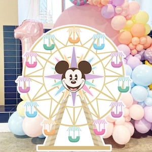 May include: A decorative cutout of a Ferris wheel featuring a central Mickey Mouse head illustration. The wheel has gold-toned spokes and pastel-colored passenger gondolas with striped roofs in shades of pink, blue, and orange, set against a white background.