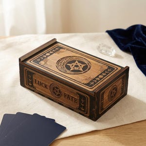 May include: A rectangular wooden box with a dark brown finish, featuring a sliding lid engraved with a central pentagram and crescent moon design. The side of the box displays the word LUCK and FATE with circular pentagram motifs and moon phases.