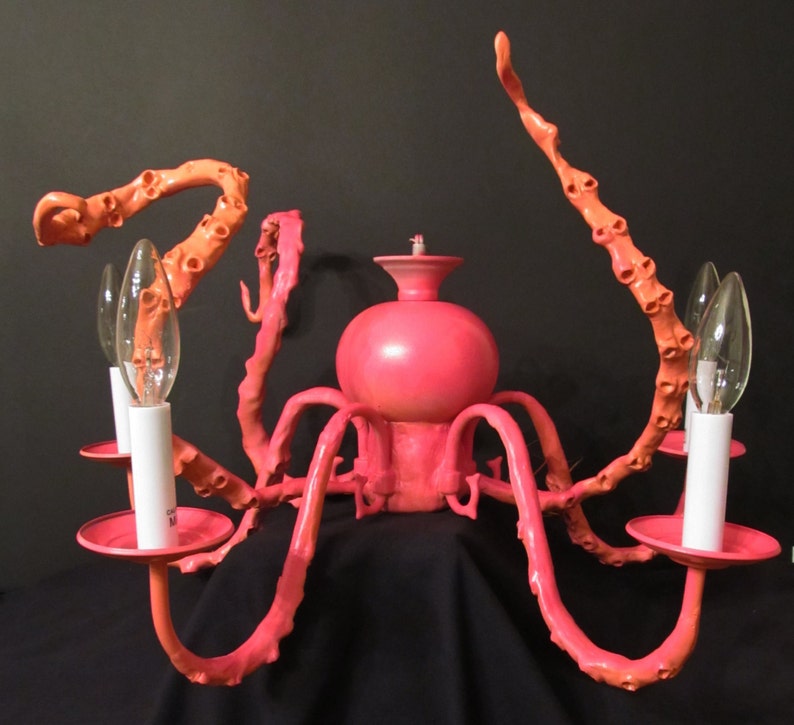 May include: A pink octopus-shaped chandelier with eight arms and six light bulbs. The chandelier is made of metal and has a pink finish.