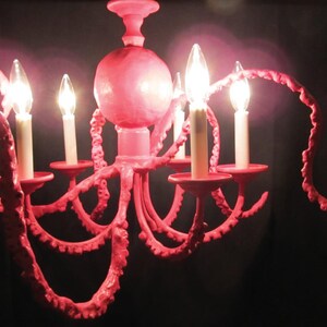 May include: A pink octopus-shaped chandelier with six light bulbs. The chandelier is made of metal and has a textured surface.