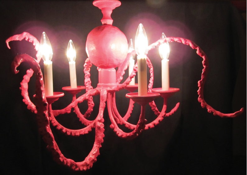 May include: A pink octopus-shaped chandelier with six light bulbs. The chandelier is made of metal and has a textured surface.