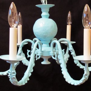 May include: A light blue chandelier with six arms, each ending in a white candle holder. The chandelier has a textured, round center piece.