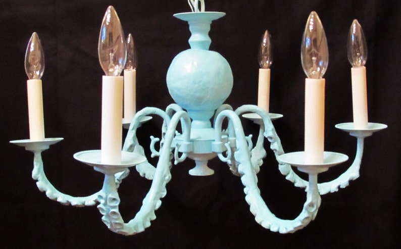 May include: A light blue chandelier with six arms, each ending in a white candle holder. The chandelier has a textured, round center piece.
