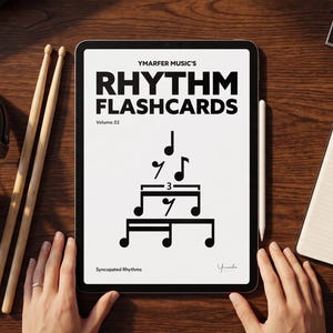 May include: A tablet displaying Ymarfer Music's Rhythm Flashcards Volume 02 with a pyramid of musical notes and the text Syncopated Rhythms. The tablet is surrounded by black headphones, two wooden drumsticks, and an open notebook with musical notation.