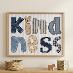 Op de afbeelding: Een ingelijste kunstdruk met het woord KINDNESS, gespeld in verschillende stoffen texturen en patronen, waaronder denim, beige met hartjes, blauwe strepen en blauwe ruitjes, tegen een lichtblauwe en witte verticaal gestreepte achtergrond.