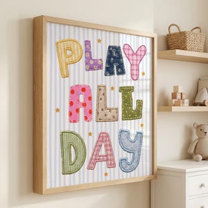 Puede incluir: Un cuadro decorativo enmarcado con el texto PLAY ALL DAY en letras coloridas con patrones de tela sobre un fondo de rayas verticales azul claro y blanco, decorado con pequeñas estrellas amarillas distribuidas por la imagen.