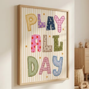 Pode incluir: Uma impressão de arte emoldurada com o texto PLAY ALL DAY em letras grandes, multicoloridas e estampadas que lembram retalhos de tecido com costuras visíveis. O fundo tem listras verticais creme e brancas com pequenas estrelas douradas.
