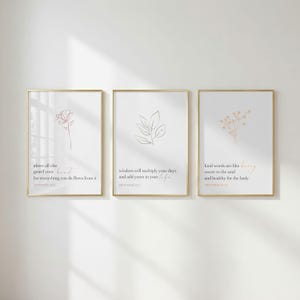 以下が含まれることがあります： ゴールドのフレームに入った3枚の縦型ウォールアートプリント。白い背景に花、葉、小枝のミニマルな線画が描かれています。各プリントには、箴言からの聖句が黒とオレンジの文字で記されています。