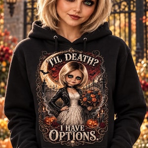 Puede incluir: Una sudadera negra con capucha que presenta un estampado gráfico de una muñeca con vestido blanco y chaqueta de cuero negra sosteniendo un ramo de flores. El texto dice TIL DEATH? I HAVE OPTIONS. El diseño incluye calabazas, velas y una luna llena.