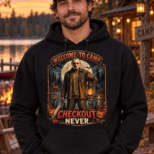 Puede incluir: Una sudadera negra con capucha que presenta un estampado gráfico de una figura con máscara de hockey sosteniendo una linterna y un machete. El texto dice Welcome to Camp y Checkout Never. El diseño incluye luna llena, bosque, cabañas y calabazas.