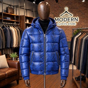 May include: A bright blue puffer jacket with a black snakeskin pattern, featuring a hood, a full-length front zip, and two zipped side pockets. The jacket is displayed on a mannequin wearing a black turtleneck underneath in a retail store.