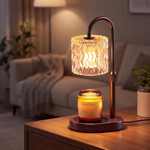 May include: A dark brown metal candle warmer lamp with an adjustable neck and a cylindrical, wavy-textured glass shade. The lamp illuminates a glass jar candle labeled Grapefruit & Bergamot, which sits on the circular base of the device.