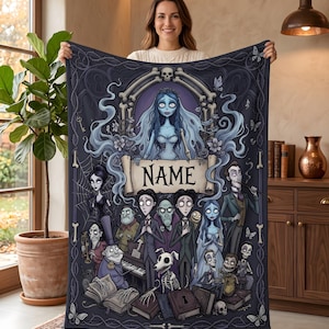 May include: A rectangular fleece blanket featuring a dark, gothic-inspired illustration of various animated characters, including a central blue-skinned bride figure above a scroll with the text NAME, surrounded by skeletal motifs and butterflies.