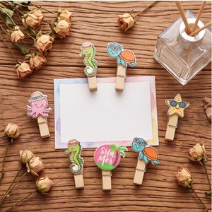 May include: A set of six wooden clothespins featuring colorful cartoon sea creatures including a pink octopus, green seahorses, blue turtles, a yellow starfish, and a circular pink sign with the text "SUN MER" attached to a white rectangular card.