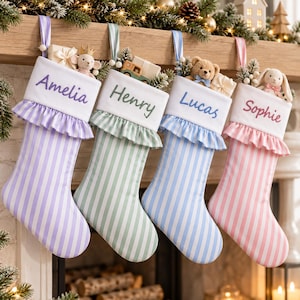 Puede incluir: Cuatro calcetines navideños a rayas con puños blancos que llevan bordados los nombres Amelia, Henry, Lucas y Sophie. Cada calcetín tiene un borde con volantes y está relleno de pequeños juguetes y regalos, como un ratón, un camión y un oso.