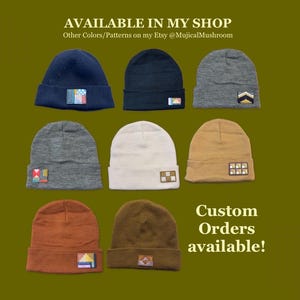 May include: Eight knit beanies in various colours including navy, black, grey, white, tan, rust, and brown. Each beanie features a small, rectangular, embroidered patch with unique geometric patterns on the front cuff. Text reads: AVAILABLE IN MY SHOP, Other Colours/Patterns on my Etsy @MujicalMushroom, Custom Orders available!