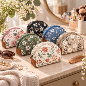 May include: A collection of six semi-circular cosmetic pouches featuring various floral patterns in black, white, blue, green, and beige, each with a brown base, a top zipper closure, and a structured design for organizing small personal items.