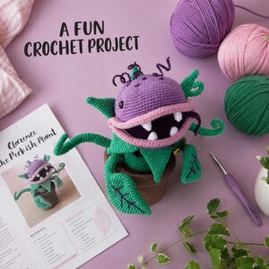 May include: A crocheted purple and green monster plant in a brown pot, featuring a wide mouth with white teeth, curly tendrils, and dark purple accents. The text A FUN CROCHET PROJECT and Clarence The Peckish Plant appear on the page.