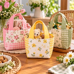 Op de afbeelding: Drie kleine stoffen draagtassen met hengsels, elk met een uniek patroon. De roze tas heeft bloemenprints en vichy-ruitjes, de gele tas toont gele bloemen en vichy-ruitjes, en de groene tas heeft bloemenprints en groene vichy-ruitjes.