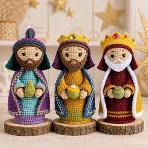 May include: Three crocheted figures representing the Three Wise Men, each standing on a circular wooden base. They feature detailed yarn work, colourful robes in purple, blue, yellow, and maroon, crowns with embedded gems, and small gifts held in their hands.