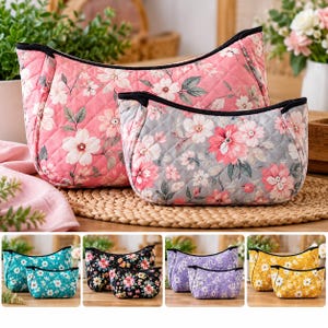 May include: A set of two quilted pouches featuring a floral pattern. The larger pouch has a pink background, while the smaller one has a gray background. Both have black zippers and a diamond-stitched texture with white and pink flower prints.