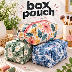 Op de afbeelding: Drie rechthoekige box-etuis met bloemenpatronen. Het bovenste etui is wit met roze en gele bloemen, het linkeronder is saliegroen met witte madeliefjes en het rechteronder is blauw met witte bloemen. Elk etui heeft een rits en een zijhandvat.