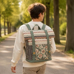 May include: A roll-top backpack featuring a mix of patterns including a floral print in muted green and brown tones, a black and white geometric section, and horizontal striped bands. The bag has solid green straps and two small wooden buttons.