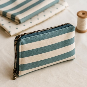May include: A rectangular zippered pouch featuring a pattern of horizontal teal and off-white stripes. The pouch has a dark teal fabric gusset and a metallic bronze-toned zipper pull. The construction is made of a sturdy textile material.