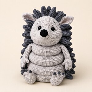 May include: A crochet hedgehog toy featuring a light grey body and dark grey spines. The figure has a round head with black bead eyes, a black nose, and a segmented torso. It has two arms, two feet with small claws, and pointed ears.