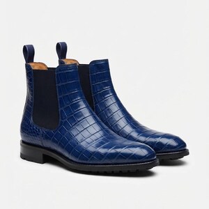 Op de afbeelding: Een paar blauwe Chelsea boots met een glanzende krokodil-reliëf lederen afwerking, donkere elastische zijpanelen en bijpassende blauwe treklipjes aan de bovenkant. De laarzen hebben een zwarte zool met profiel en een lage blokhak.