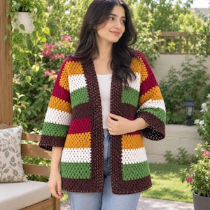 May include: A crochet cardigan featuring a granny square pattern with horizontal stripes in dark brown, mustard yellow, white, and olive green. The garment has an open front, three-quarter length sleeves, and a straight hemline, worn over a white top.