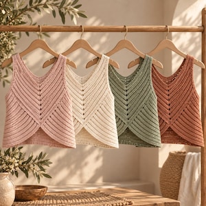 May include: Four sleeveless crochet tank tops hanging on wooden hangers. The tops feature a V-neckline and a textured chevron pattern. The colors from left to right are dusty pink, cream, sage green, and terracotta orange, all with a cropped length.