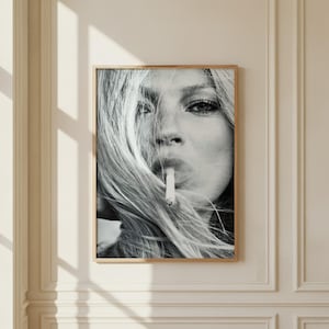 Könnte beinhalten: Ein schwarz-weißes Wandkunst-Fotodruck-Bild in einem dünnen Holzrahmen. Das Bild zeigt ein Nahaufnahme-Porträt einer Person mit langem, fließendem Haar, das das Gesicht teilweise verdeckt, und einer Zigarette zwischen den Lippen.