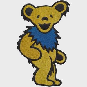 May include: Embroidered patch featuring a yellow bear with a blue collar and black accents. The bear is smiling and standing upright. This patch is suitable for jackets, bags, or other fabric items.