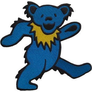 May include: A blue bear patch with a yellow collar and black outlines. The bear is in a running pose with a smiling face. The patch is embroidered with a textured appearance.