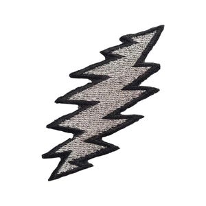 May include: Embroidered patch in the shape of a silver lightning bolt with a black border. The patch has a textured appearance, and the lightning bolt design is centered on a white background.