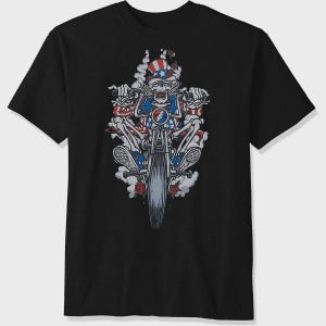 May include: Black t-shirt featuring a skeleton riding a motorcycle. The skeleton is adorned with patriotic stars and stripes, wearing a hat and surrounded by smoke and roses. The motorcycle has a blue and red emblem.