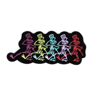May include: An embroidered patch featuring five dancing skeletons in a line, each wearing a top hat and holding a cane. The skeletons are in different colors: purple, green, light blue, pink, and red.