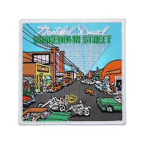 May include: A colorful embroidered patch featuring a street scene with buildings, cars, and motorcycles. The text "The Grateful Dead" and "Shakedown Street" is visible on the patch.