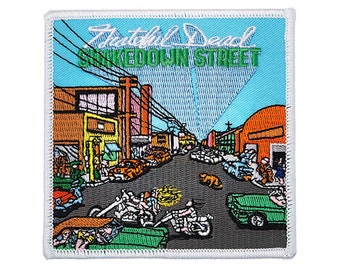 May include: A colorful embroidered patch featuring a street scene with buildings, cars, and motorcycles. The text "The Grateful Dead" and "Shakedown Street" is visible on the patch.