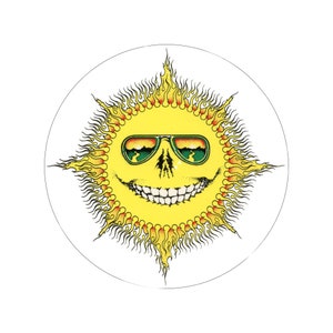 May include: A circular graphic featuring a smiling sun with sunglasses. The sun is yellow with orange and red flames radiating outwards. The sunglasses have green lenses with a landscape design. The sun's face has a skull-like appearance.