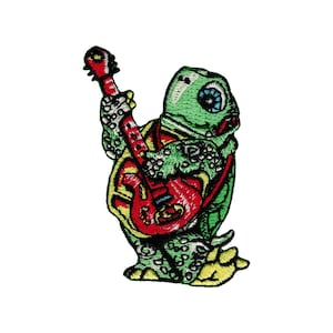 May include: An embroidered patch of a green turtle playing a red electric guitar. The turtle has a yellow shell with black spots and a blue eye.